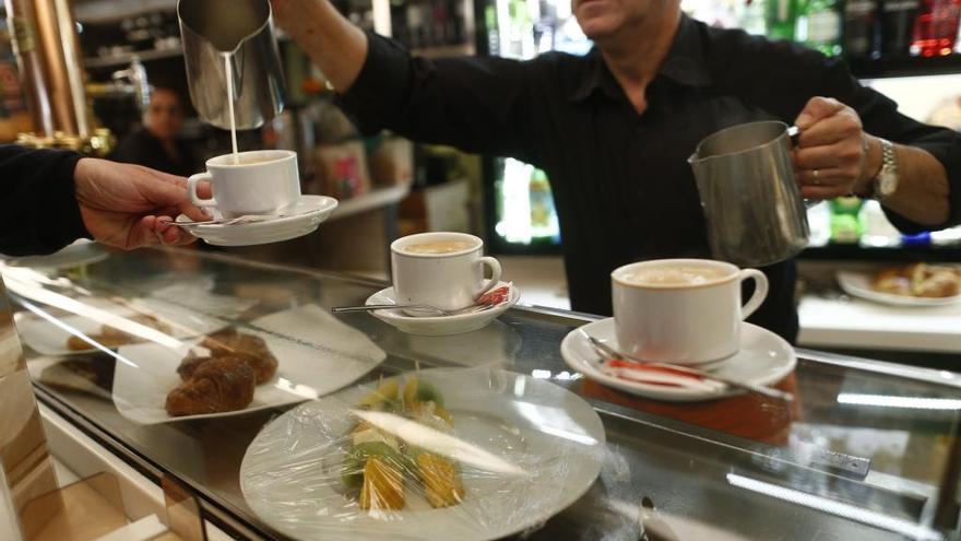 Un camarero sirve a un cliente un café con leche.