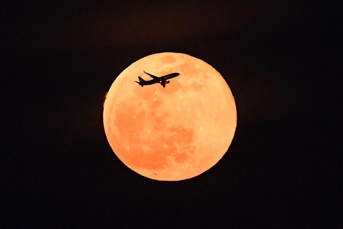 A plane fly past the full moon, also known as the Hunter’s Moon, in Singapore on October 7, 2025. (Photo by Roslan RAHMAN / AFP)