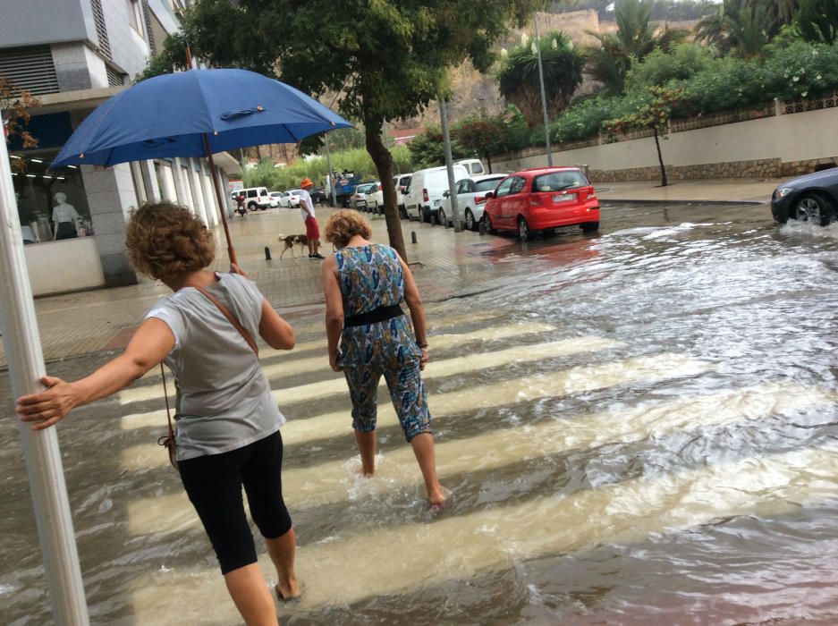 Los peatones tratan de cruzar por las calles anegadas de agua en Dénia.