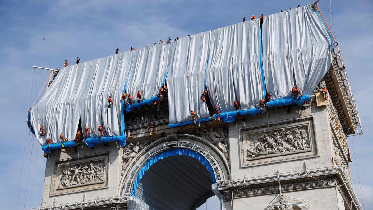 Workers unravel silver blue fabric, part of the process of wrapping L'Arc de Triomphe in Paris on September 12, 2021, designed by the late artist Christo. - Work has begun on wrapping the Arc de Triomphe in Paris in silvery-blue fabric as a posthumous tribute to the artist Christo, who had dreamt of the project for decades. Bulgarian-born Christo, a longtime Paris resident, had plans for sheathing the imposing war memorial at the top of the Champs-Elysees while renting an apartment near it in the 1960s. (Photo by Thomas SAMSON / AFP) / RESTRICTED TO EDITORIAL USE - MANDATORY MENTION OF THE ARTIST UPON PUBLICATION - TO ILLUSTRATE THE EVENT AS SPECIFIED IN THE CAPTION