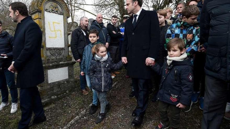 Macron pasa ante una tumba profanada con una esvástica en el cementerio de Quatzenheim. // Reuters