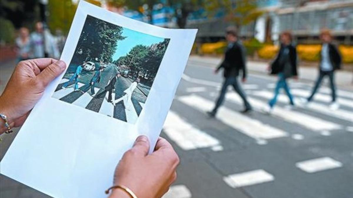 Una turista contempla una fotocopia de la portada del disco 'Abbey Road' ante el célebre paso de cebra perpetuado por los Beatles.