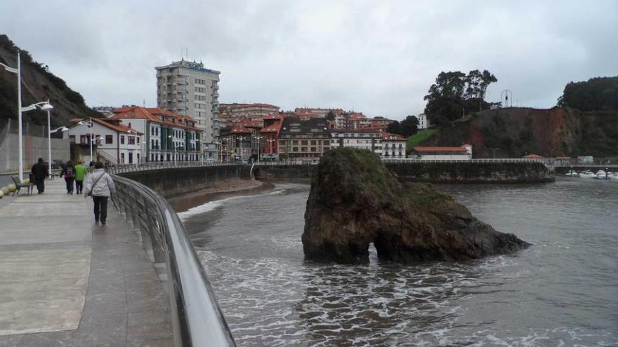 Varias personas caminan por el paseo marítimo de Candás, a la altura de la Peña Furada.