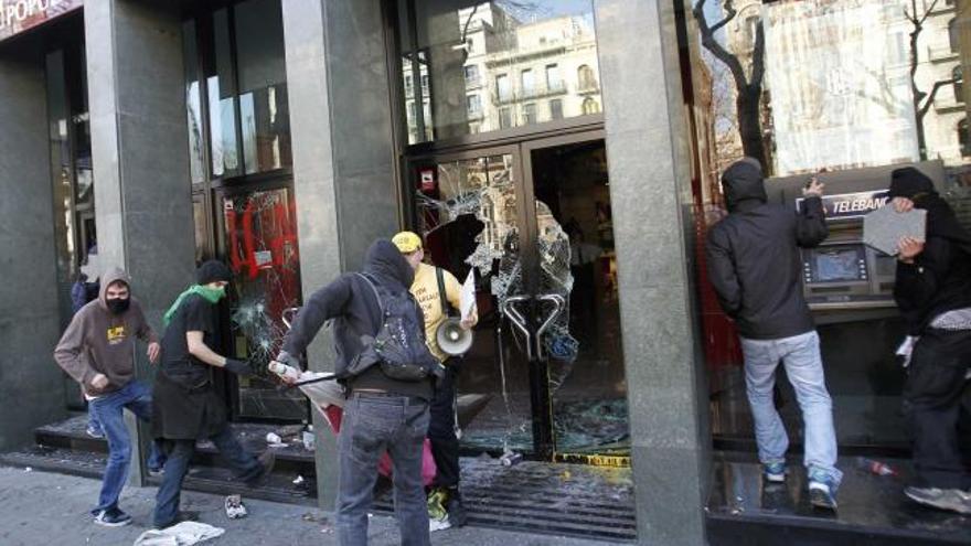 Grupos de violentos atacan los escaparates de una sucursal en Barcelona. A la derecha, la Policía protege a Monago.