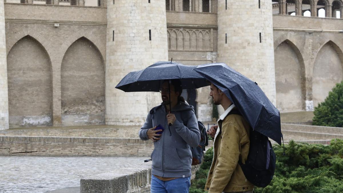 Visitantes de La Aljafería, en Zaragoza, protegiéndose de la lluvia con sus paraguas.