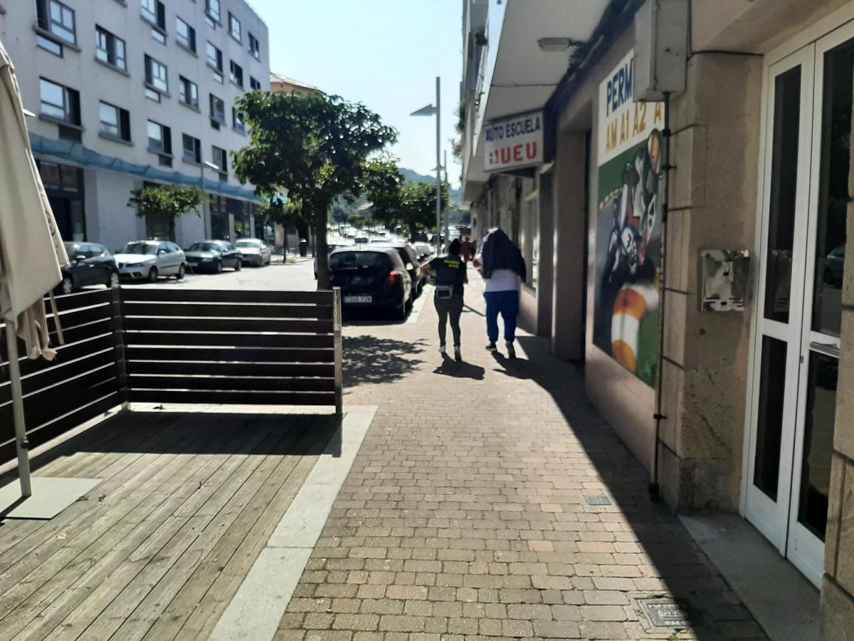Una agente de la Guardia Civil junto a uno de los investigados, que se cubre la cabeza con una chaqueta, a la salida del registro de un piso en la calle Johan Carballeira, en el centro de Bueu.