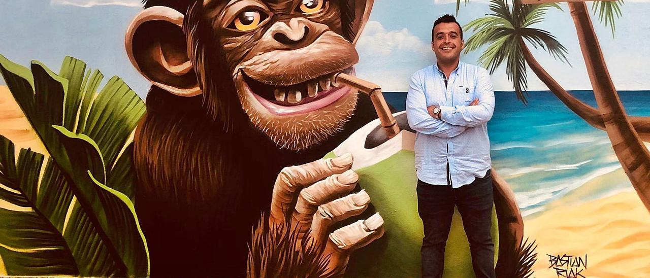 El hostelero Miguel García, más conocido como “Kiko”, justo al grafiti realizado por Bastian Riak, en el chiringuito de la  playa de San Pedro. | R. A. M. S.