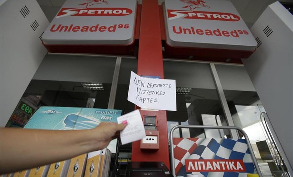 Un empleado de una gasolinera entrega un recibo frente a un cartel en el que puede leerse que no se aceptan tarjetas de crédito para el pago.