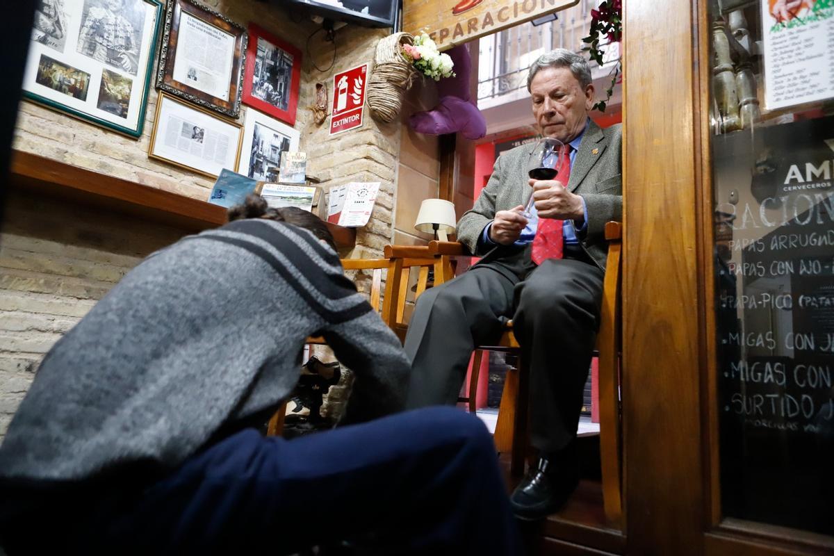Ángel Pastor lustra el calzado de un cliente mientras se relaja con una copa de vino.