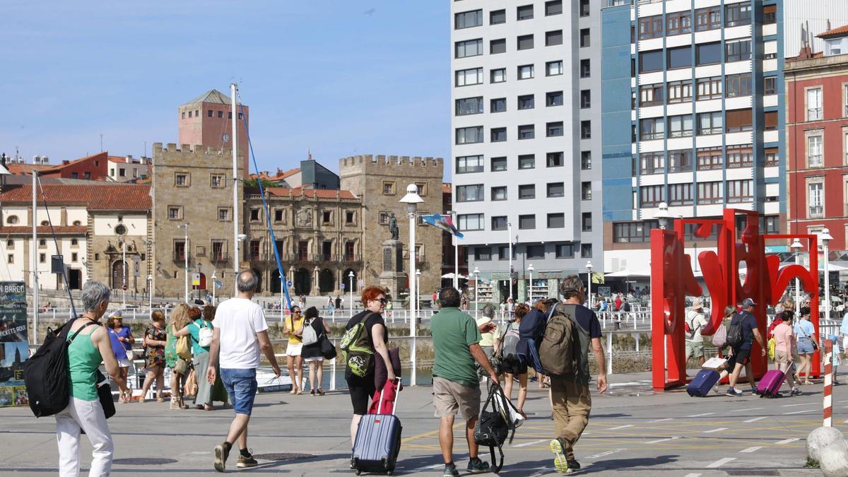 Turistas con maletas paseando por el puerto deportivo de Gijón.