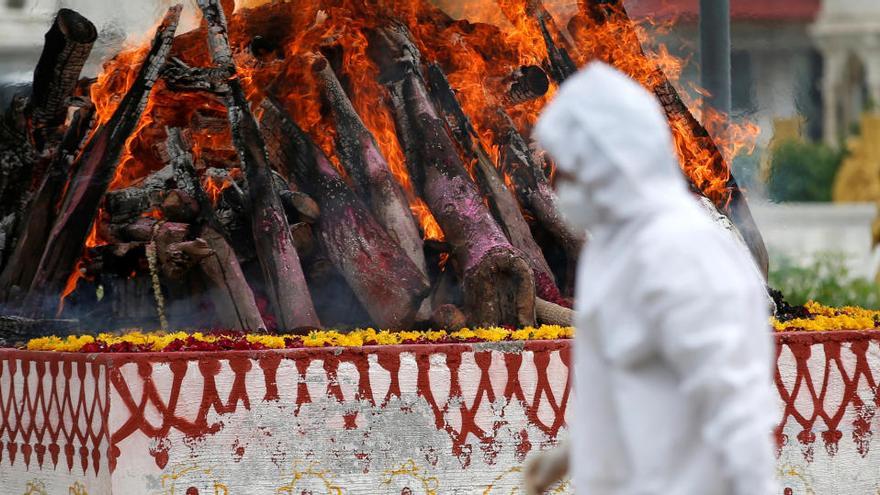 Un sanitario camina frente a una hoguera homenaje a los fallecidos, en India