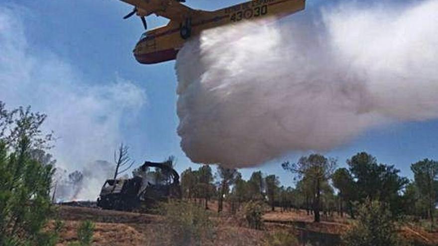 Un hidroavión descarga agua junto a la máquina astilladora que originó el incendio forestal.