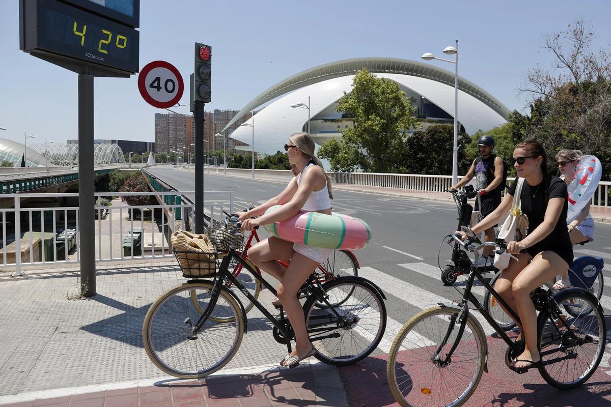 Varias jóvenes en bici al paso de un termómetro que marca 42 grados en un día del mes de julio de 2025 en València.