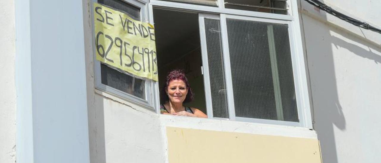 Una mujer asomada a una ventana de una vivienda en venta.