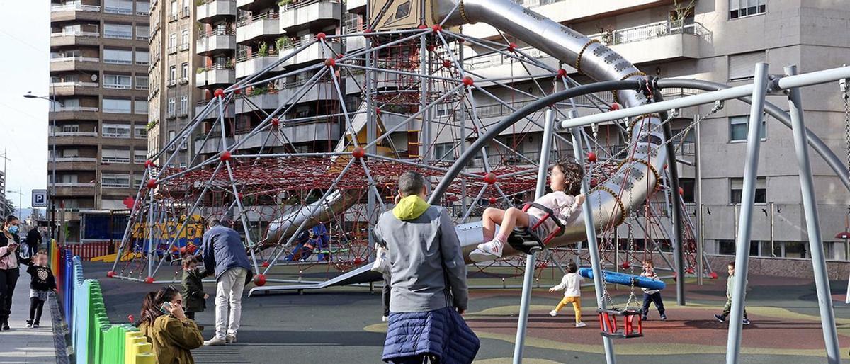 Niños jugando en el parque infantil de la calle Venezuela, supervisados por varios adultos.