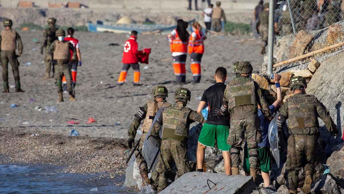 Miembros del ejército ayudan a varios inmigrantes a su llegada a la playa de El Tarajal, junto a la valla fronteriza , en Ceuta este miércoles.