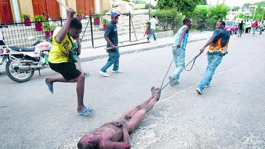 Linchamiento dantesco. Sobre estas líneas, la secuencia del horrible linchamiento de un presunto ladrón por los desesperados haitianos. En la foto de arriba, dos personas arrastran por una calle el cuerpo del hombre, mientras otra lo golpea con saña. En la del medio, un hombre golpea al saqueador, que yace en el suelo. Sobre estas líneas, el hombre es quemado vivo tras haber amontonado sobre su cuerpo todo tipo de desechos.