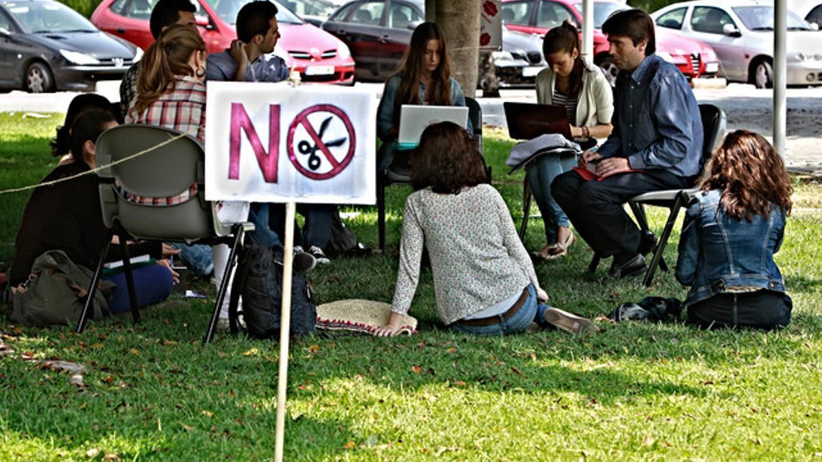 Un grupo de estudiantes da clase al aire libre junto a una camparta contra los recortes en educación