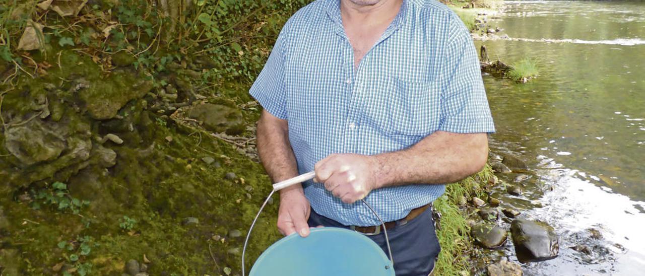 Manuel Granda muestra un cubo lleno de alevines. A la derecha, Eduardo López Villa sostiene en la mano un alevín de salmón atlántico.