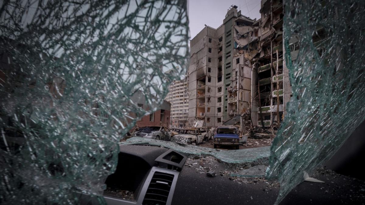 Uno de los edificios bombardeados en Kiev visto a través de la luna de un vehículo destruido.