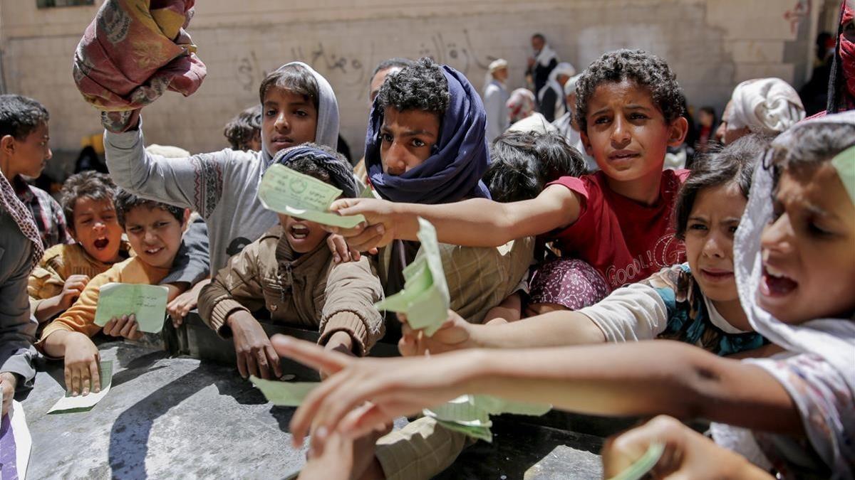 Niños yemenís presentan documentos para recibir las raciones de alimentos proporcionadas por una oenegé local en Saná