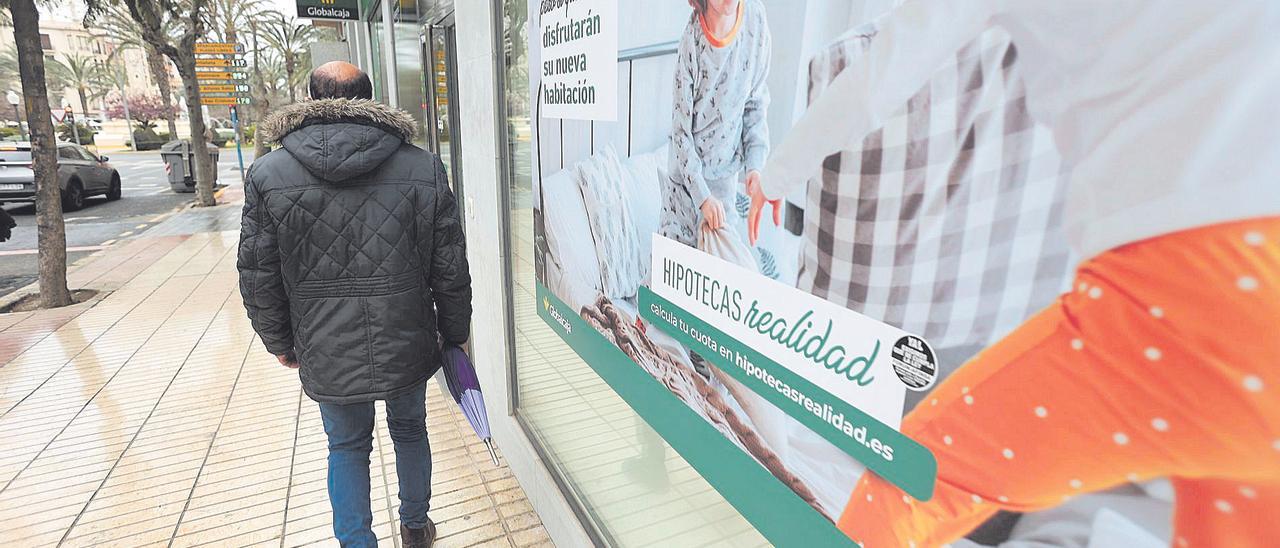 Un ciudadano camina frente a una sucursal bancaria con publicidad sobre créditos hipotecarios.