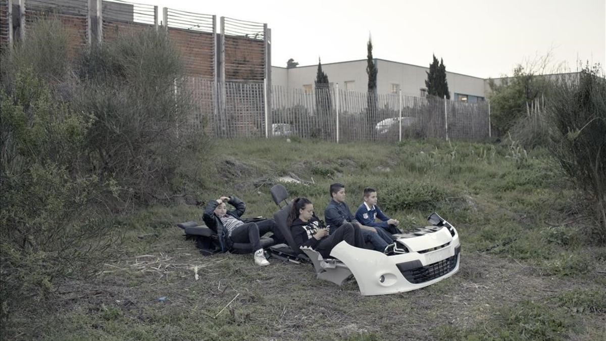 Fotografía de Arnau Bach de unos niños jugando con los restos de un coche en un descampado de Marsella, que forma parte de la exposición 'Mitos de un futuro cercano', en el Arts Santa Mònica, dentro del Docfield.