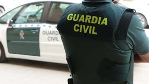 Archivo - Un agente de la Guardia Civil, de espaldas, junto a un vehículo oficial.