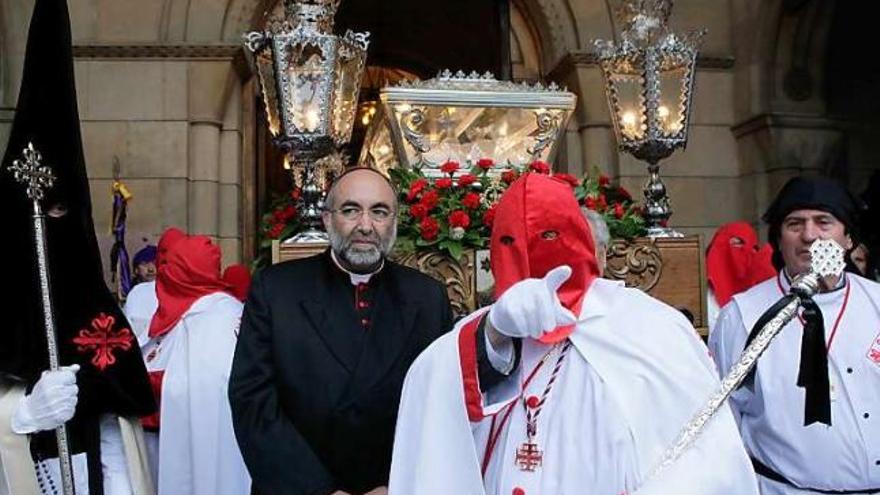 A la izquierda, el arzobispo Jesús Sanz Montes sigue la indicación de un cofrade. A la derecha, el paso del Santo Sepulcro, a la espera de salir desde el templo de San Pedro.