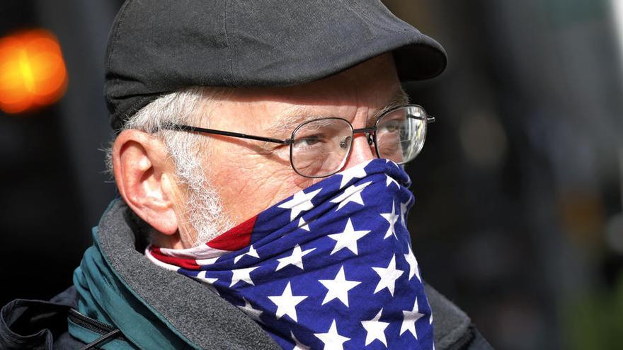 Una hombre se cubre la boca y la nariz con una prenda con la bandera estadounidense.