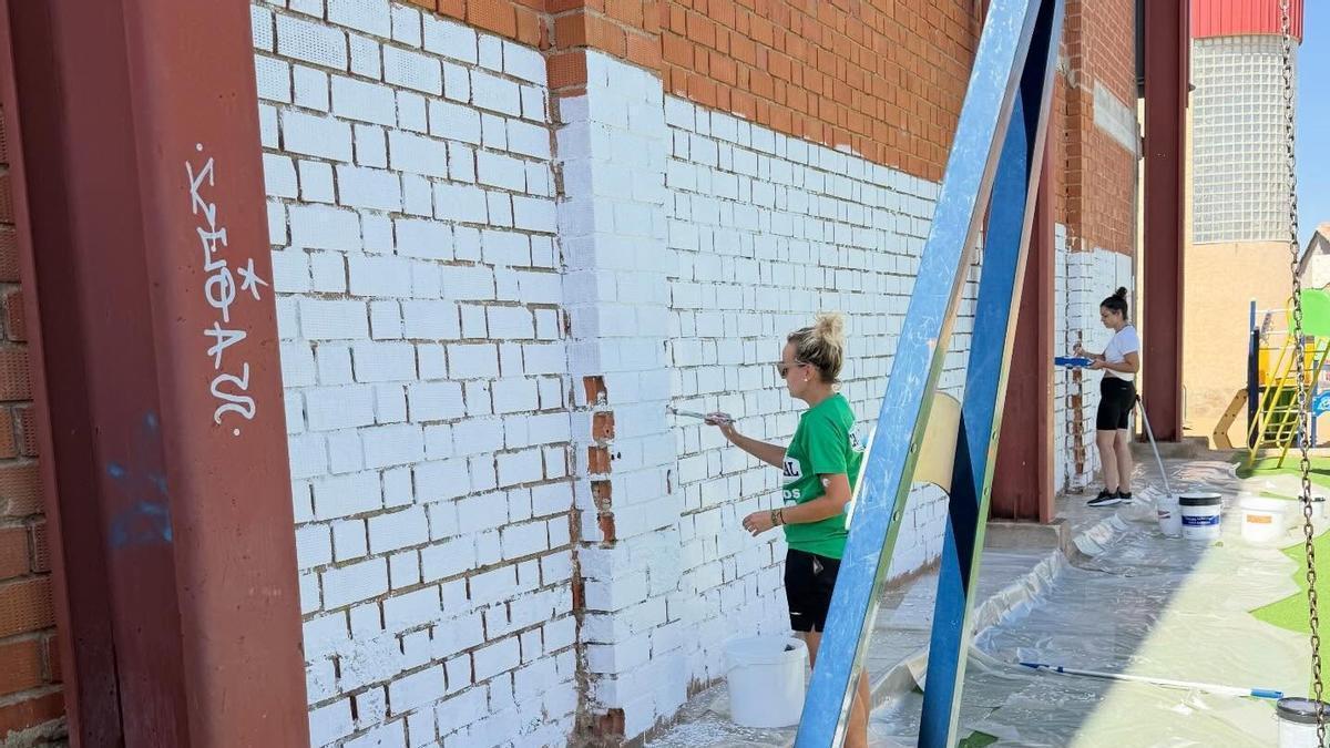 Socias del colectivo preparan la pared en la que los niños pintarán un mural durante la Semana Cultural.
