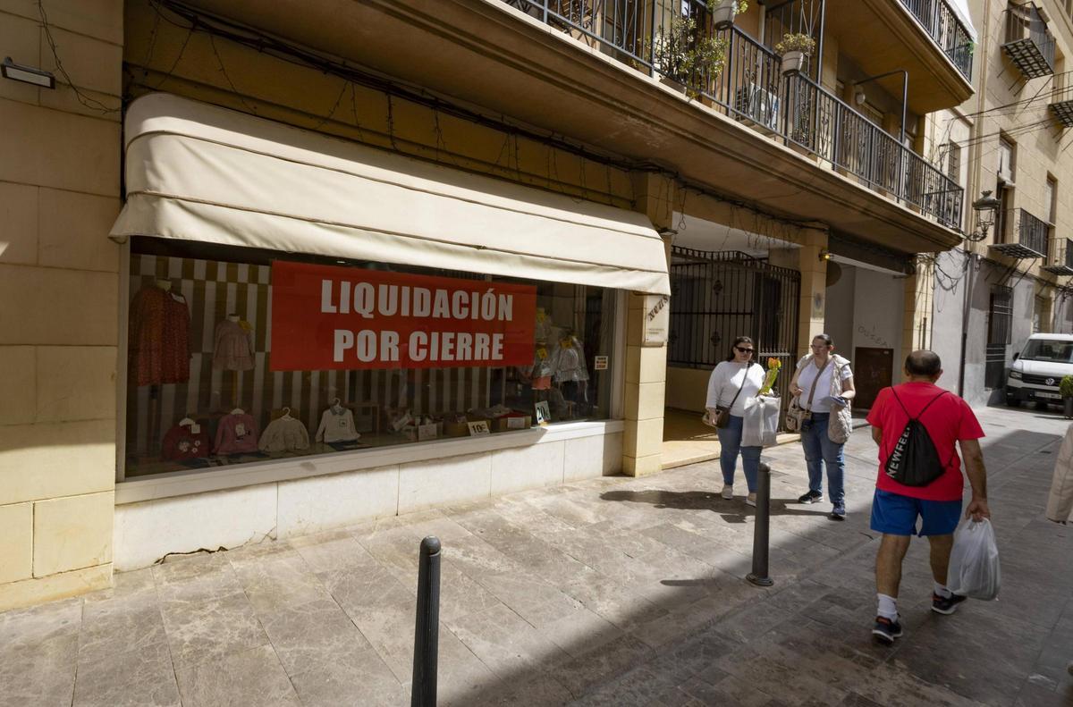 Varias personas pasan por delante del escaparate de "Neus Modes" en Xàtiva, que ha entrado en proceso de liquidación por cierre.