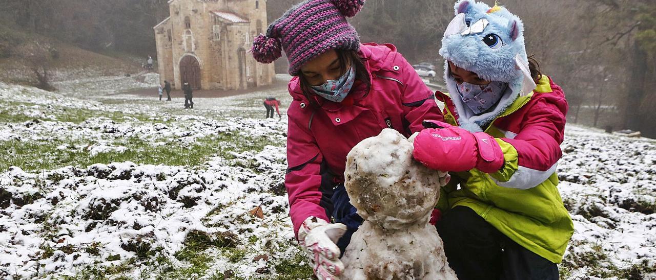 Arriba, Elsa y Lucía Ruiz haciendo un muñeco de nieve junto a San Miguel de Lillo. | Julián Rus