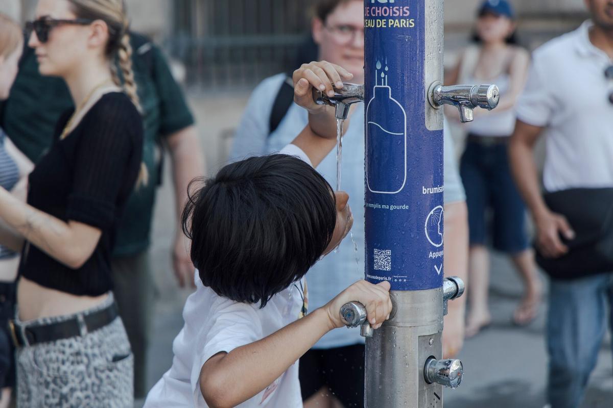 Un niño bebe agua de una fuente pública instalada en el centro de París para combatir la ola de calor.