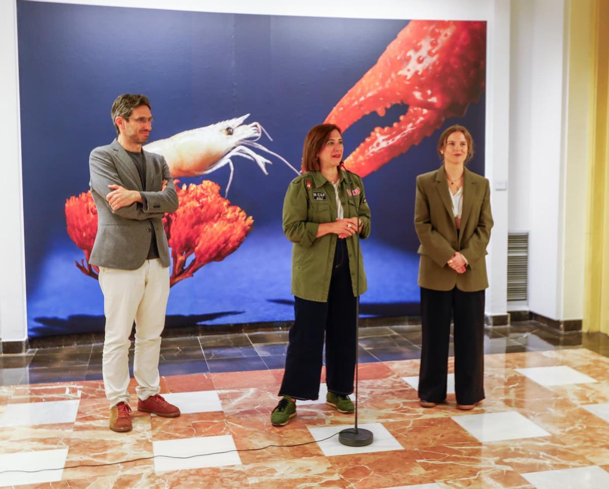 Sara Fernández, consejera de Cultura, y la fotógrafa Olga S. Ortiz con un mural de 'Crustáceo Deus' de fondo