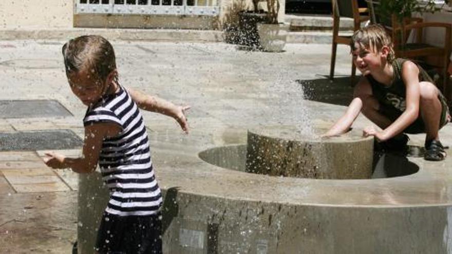 Dos niños tratan de refrescarse en una de las fuentes públicas del Centro de Málaga.