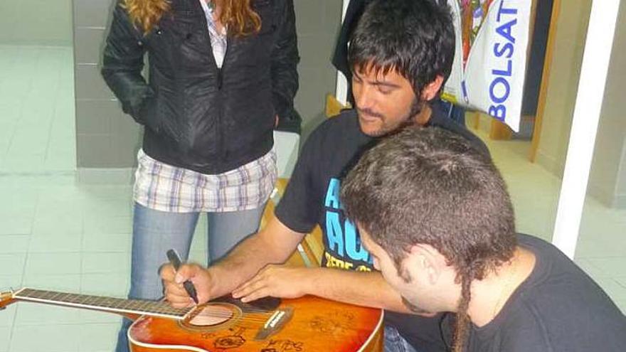 Los componentes de Estopa firmando la guitarra