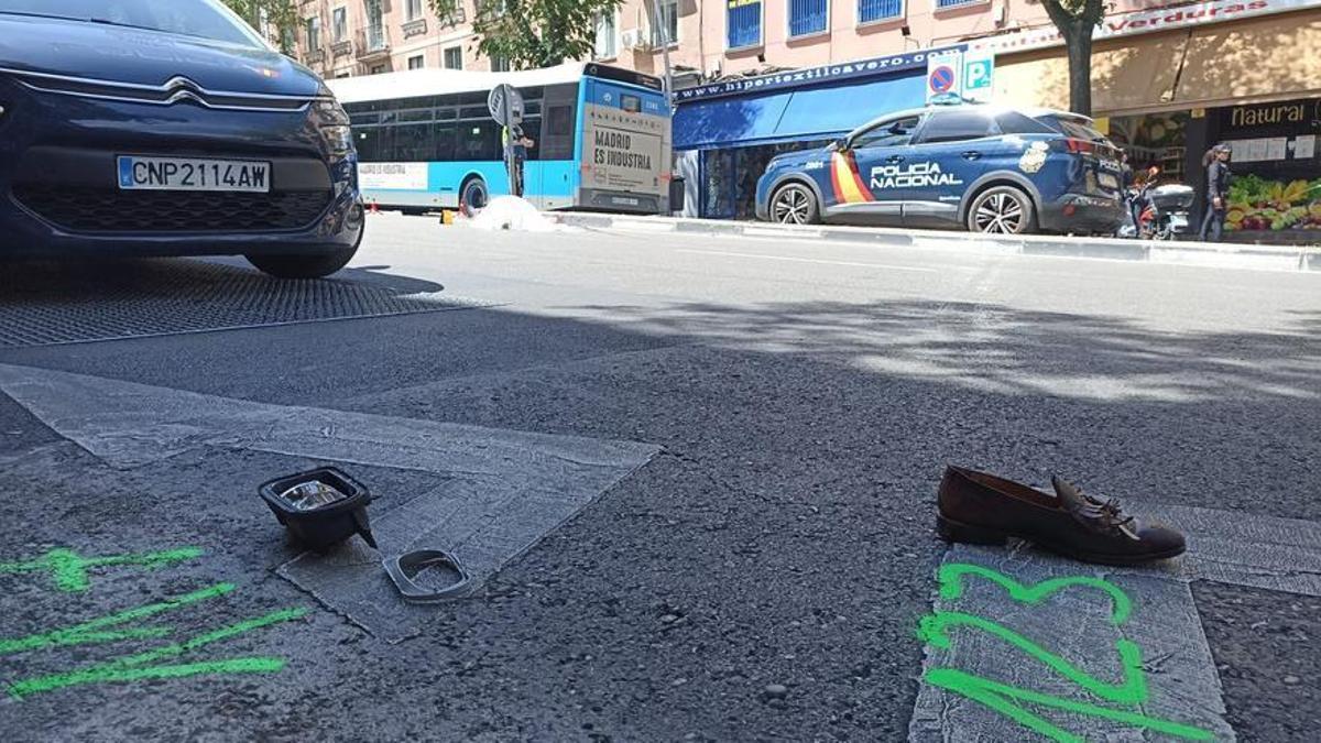 El cadáver de una de las personas atropelladas en el Paseo de Extremadura, al fondo; en primer plano, un objeto personal del fallecido y el retrovisor del coche.