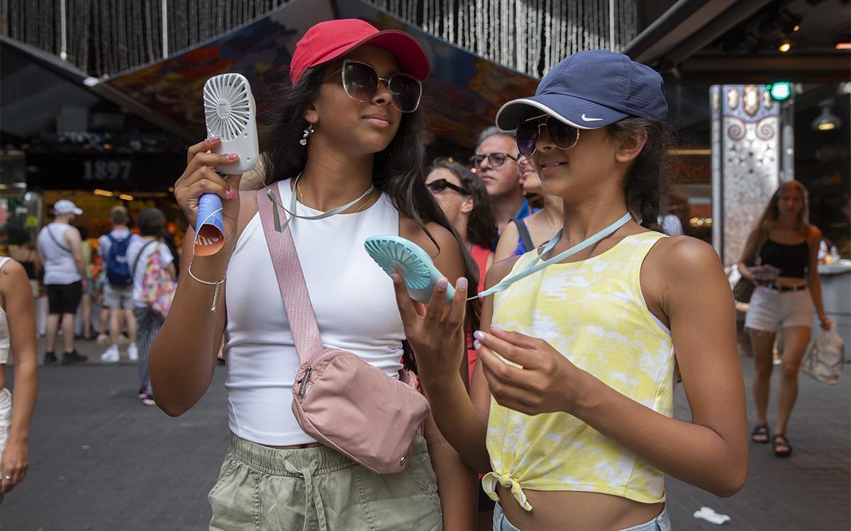 Ola de calor dos chicas de Chicago se refrescan la cara con ventiladores de mano en la boqueria Ola de calor dos chicas de Chicago se refrescan la cara con ventiladores de mano en la boqueria