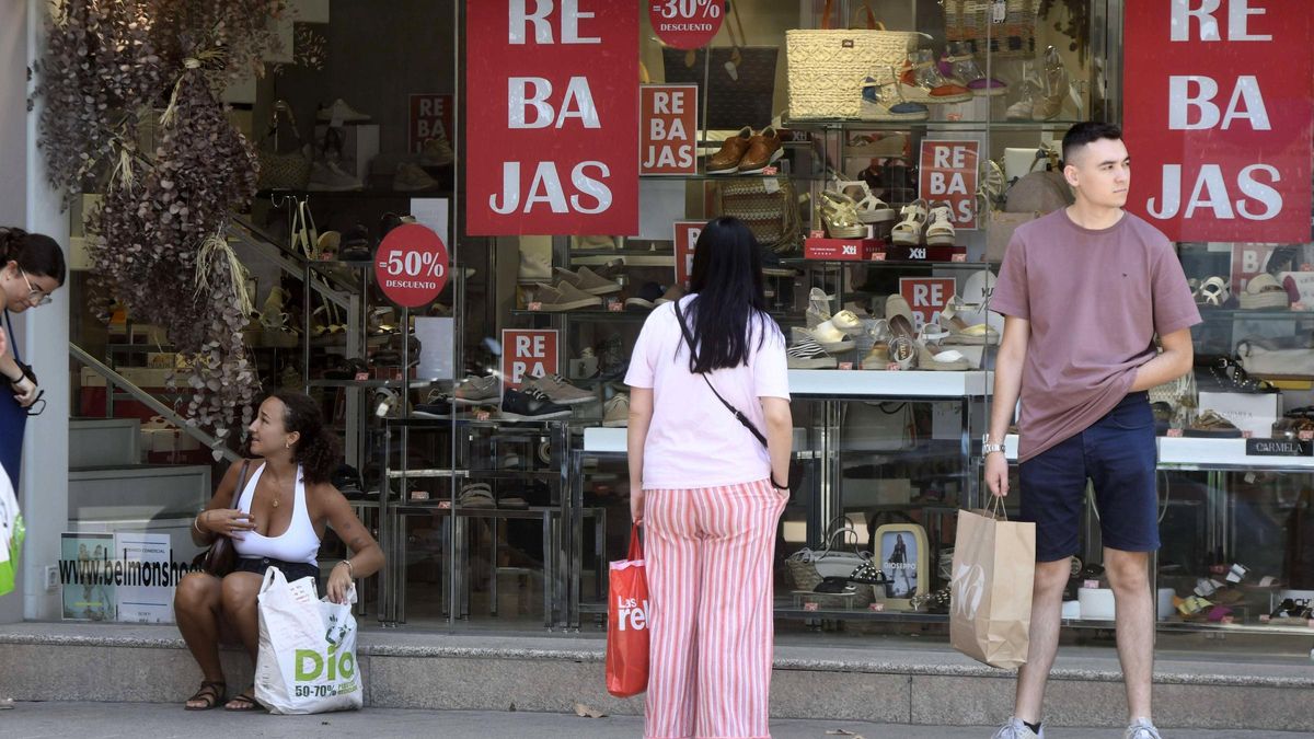 Un grupo de personas se refugia del sol a la sombra de una tienda en rebajas.