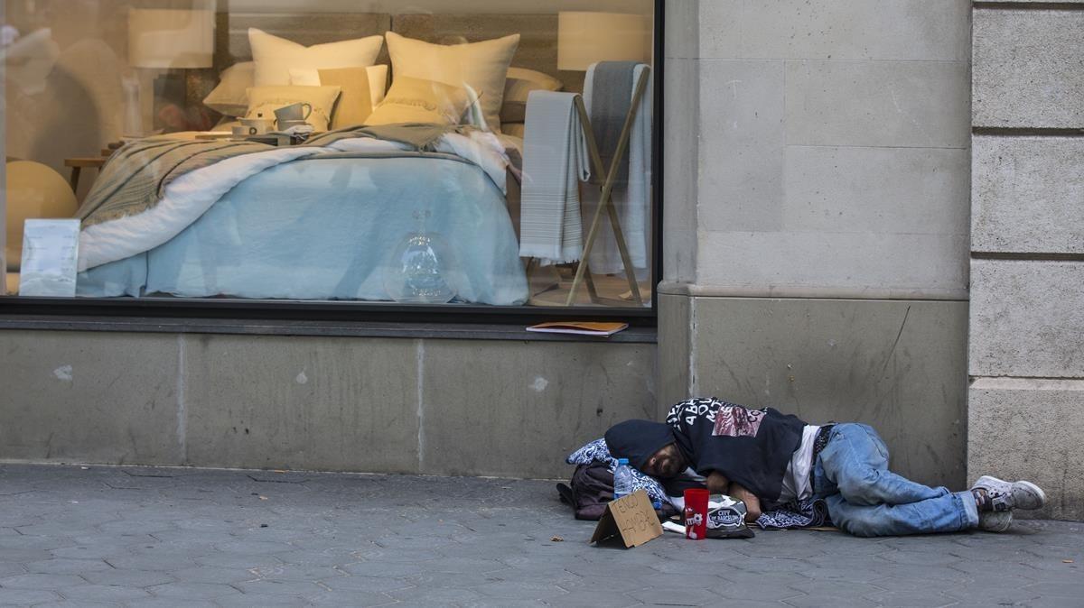 Un hombre duerme frente a un escaparate en el centro de Barcelona.