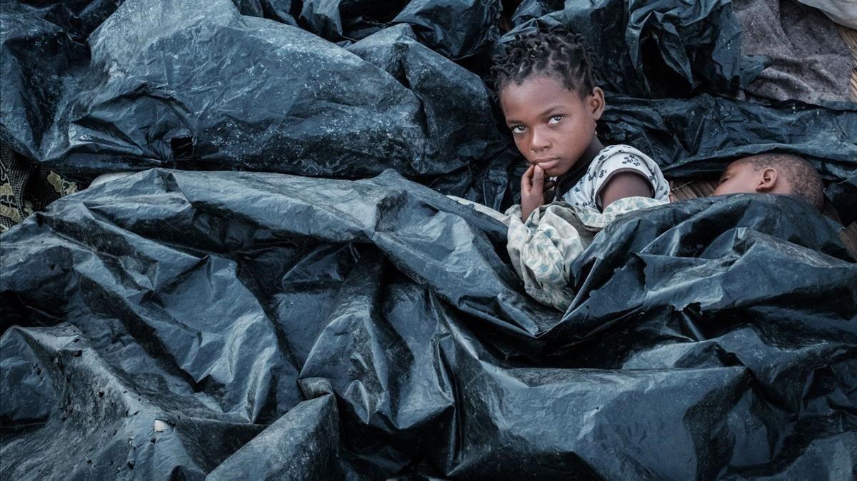 Enia Joaquin Luis se despierta junto a su hermana Luisa bajo los plástico para protegerse de la lluvia mientras se refugian en las gradas del Ring Ring en Buzi Mozambique.