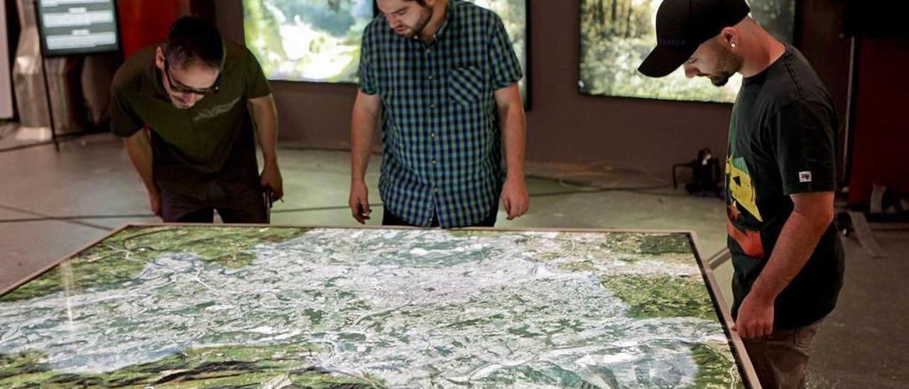 Rubén Rosón, en el centro, junto a dos organizadores, mirando uno de los mapas expuestos en el stand de Oviedo en la Feria.