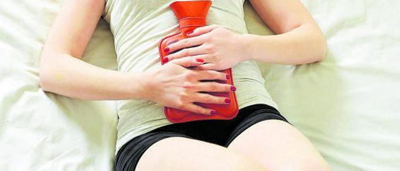 Una mujer trata de aliviar el dolor menstrual con una bolsa de agua caliente en el vientre.