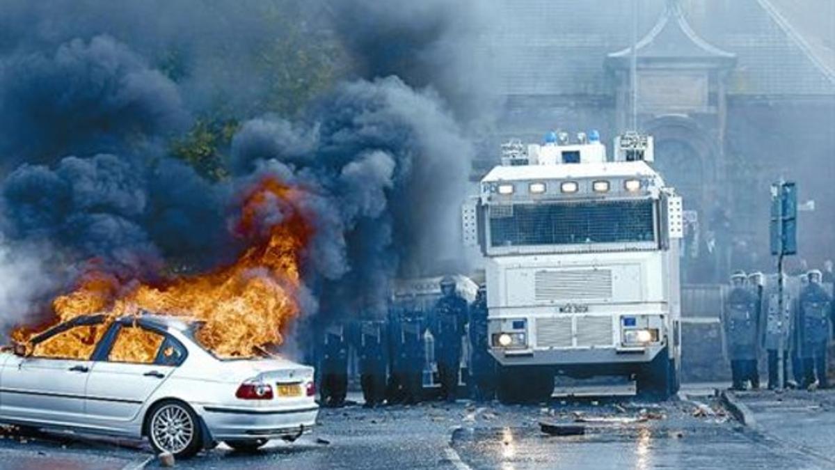 Un coche arde mientras los agentes antidisturbios observan la escena en el barrio de Ardoyne, en Belfast.