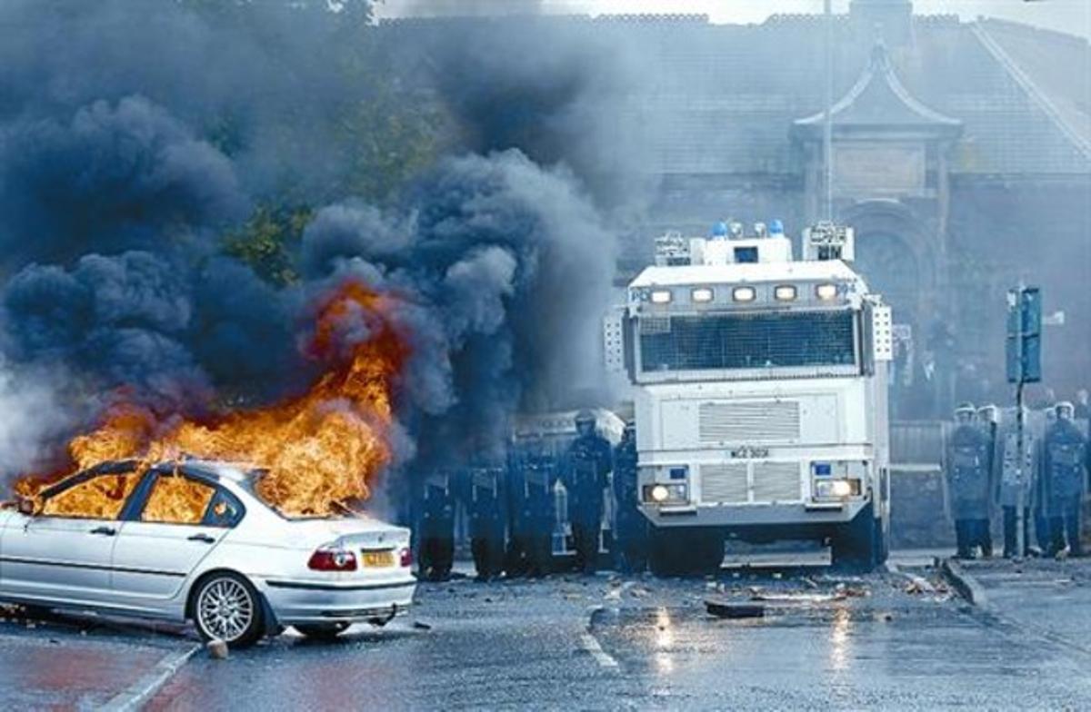 Un cotxe crema mentre els agents antiavalots observen l’escena al barri d’Ardoyne, a Belfast.