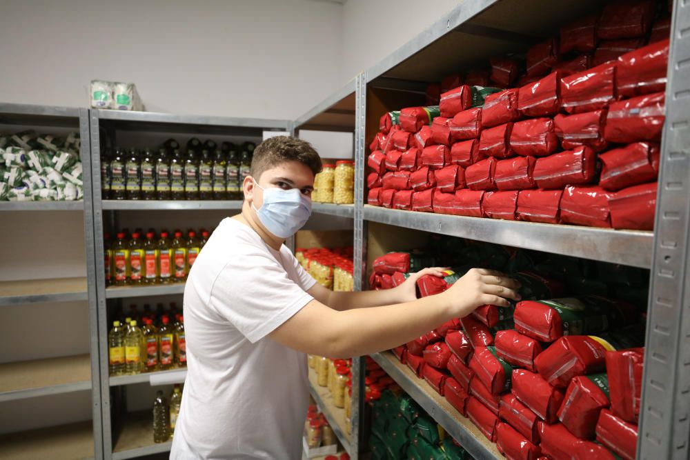 Joel Mella, un joven voluntario de  16 años, coloca unas botellas de aceite en el banco de alimentos