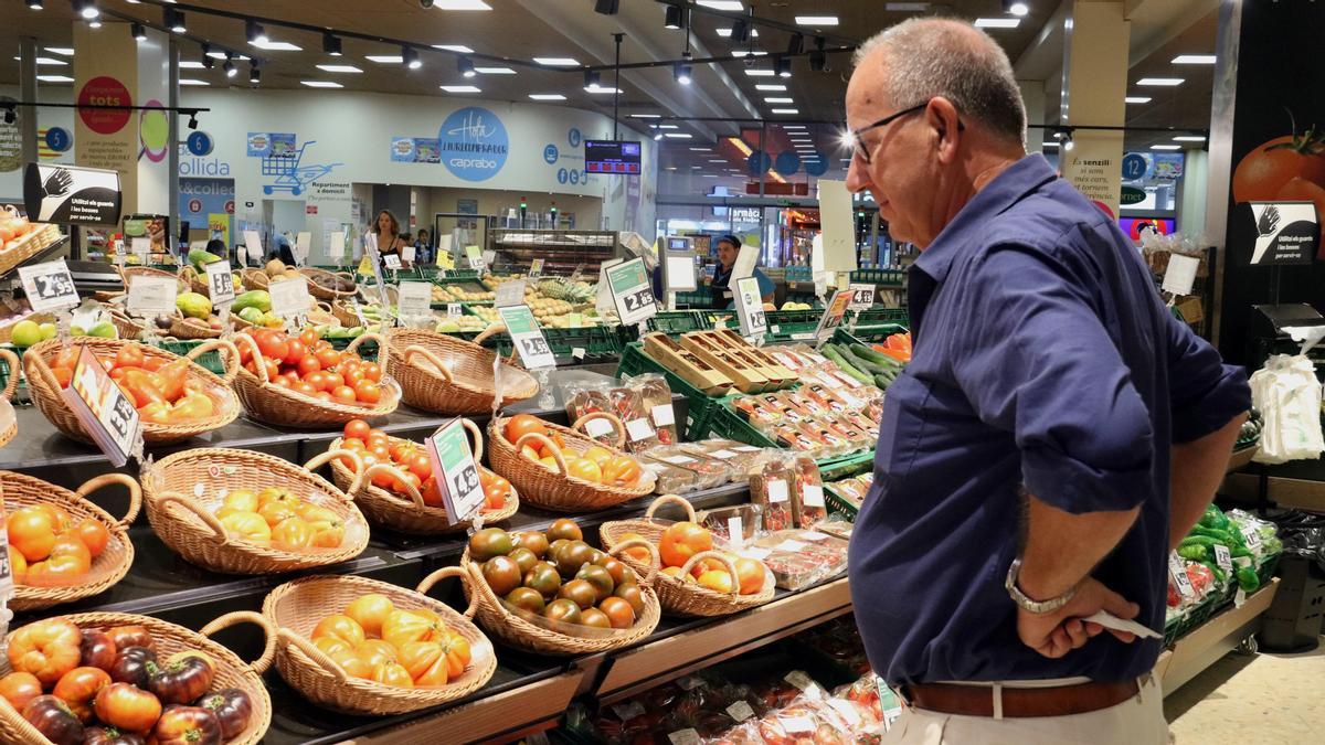 Un home compara preus de verdures en un supermercat