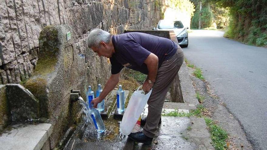 Una persona llena varias botellas de agua en la fuente de Lameira, ayer por la tarde, en Quintela. // FdV