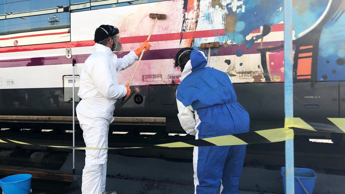 Dos operarios limpian unos grafitis en un vagón de Renfe.
